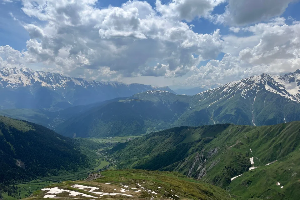 Snow-capped Caucasus peaks above a green mountain valley in Georgia.